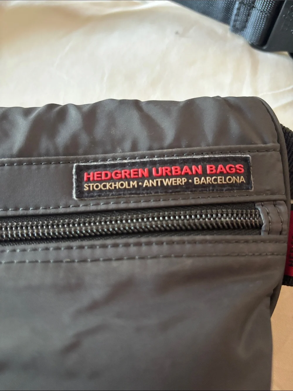 This grey Hedgren crossbody bag features a distinctive red label showcasing the